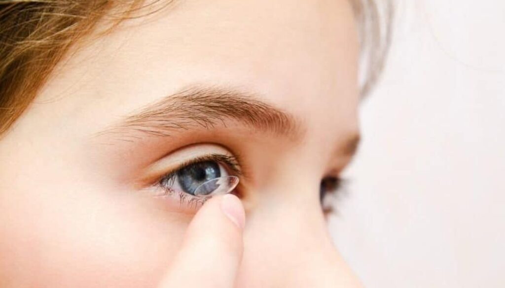 A child applying a contact lens to their eye, demonstrating the process of inserting contacts.
