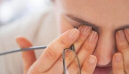 A person rubbing their eyes, possibly experiencing eye strain or dry eyes, while holding a pair of glasses.
