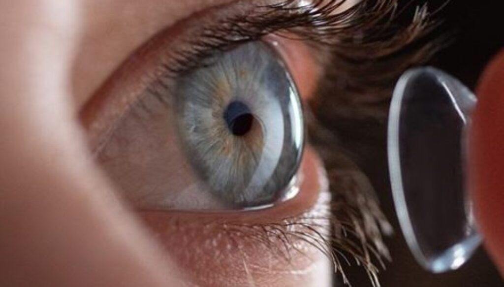 A close-up of an eye with a person inserting a contact lens, showcasing the procedure of placing contacts into the eye.