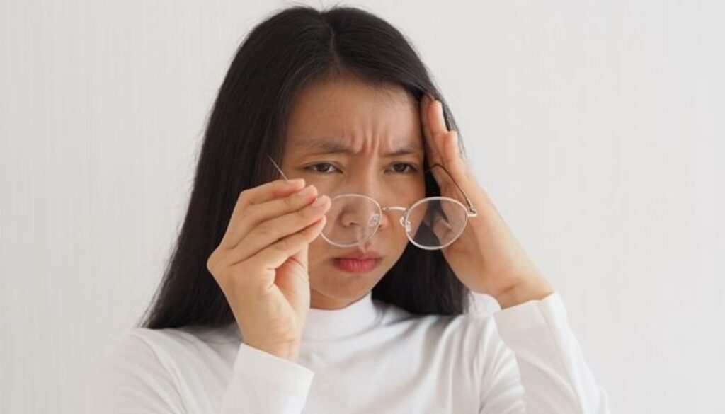 Woman holding glasses and rubbing her forehead, indicating potential eye strain or headache.